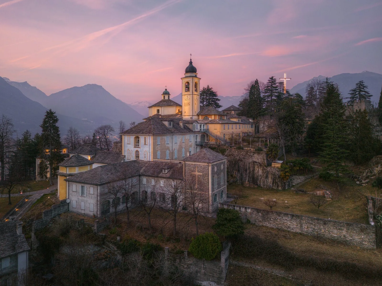Il santuario del Sacro Monte Calvario di Domodossola con il campanile illuminato al tramonto e le montagne dell'Ossola sullo sfondo