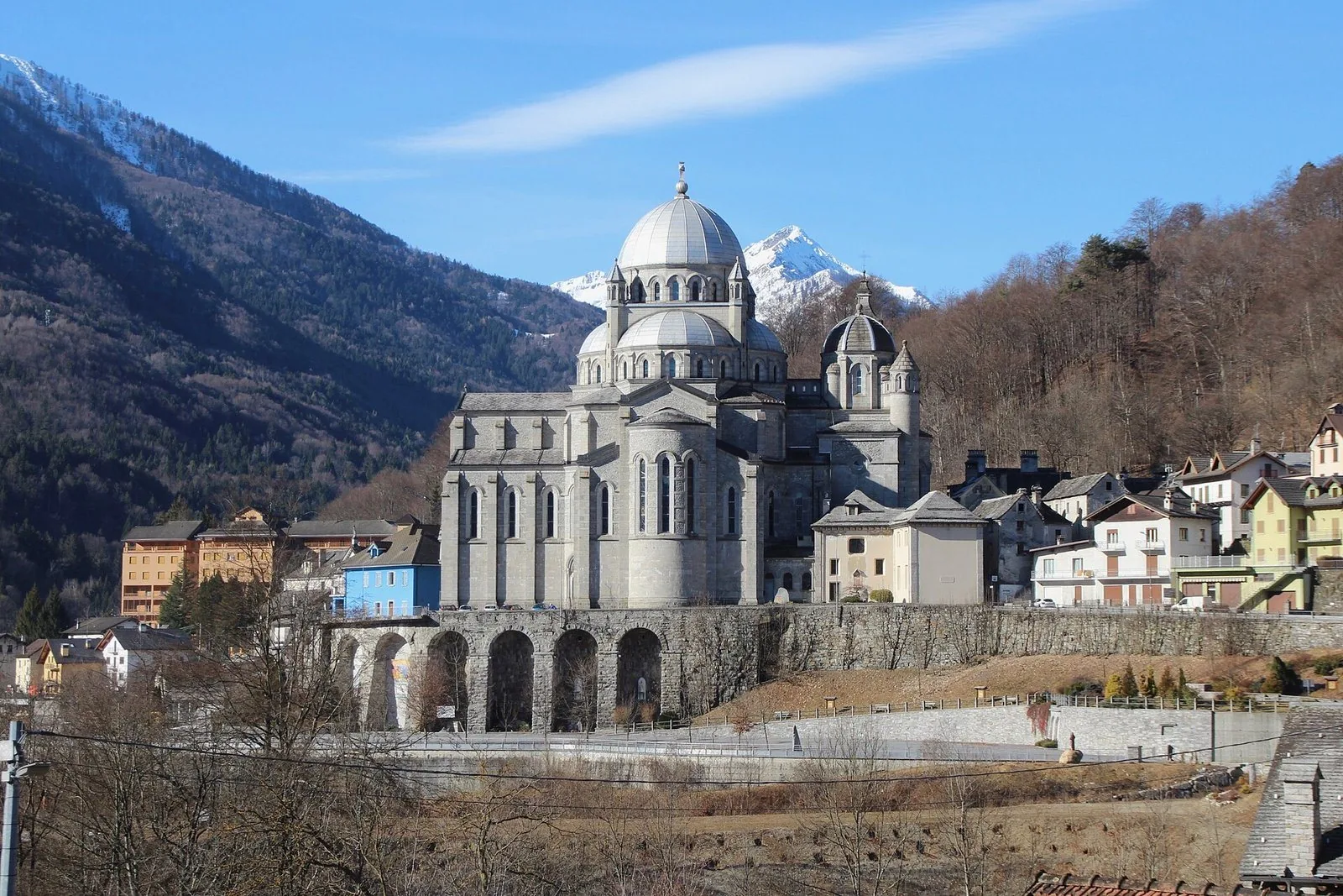 La basilica della Madonna del Sangue a Re con la grande cupola grigia, il terrapieno ad archi e le montagne innevate alle spalle